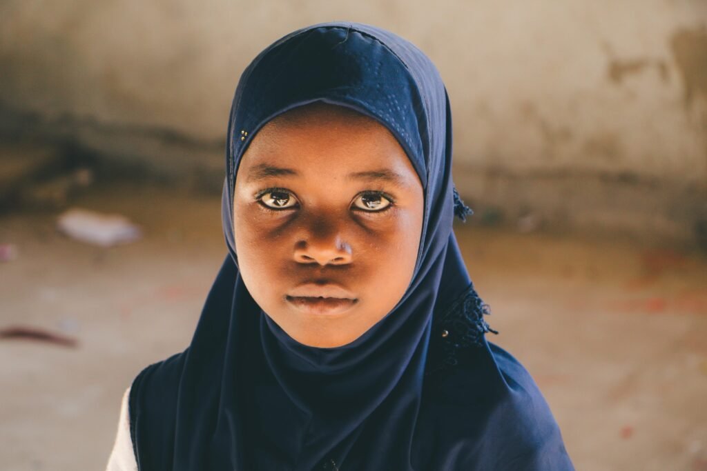 Portrait of a young girl wearing a dark blue hijab, looking serious and thoughtful.